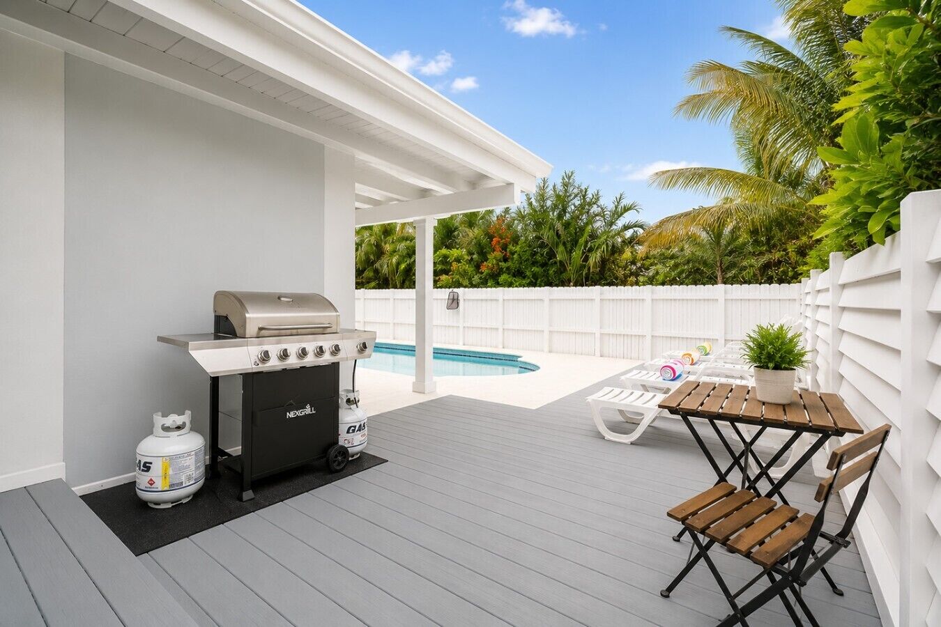 Una terraza al aire libre con una parrilla, una piscina y una mesa con sillas.
