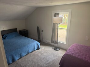 Un dormitorio con cama, ventilador, ventana con cortinas y una mesita.