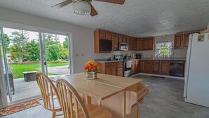 A kitchen with wooden cabinets, a central island with chairs, a refrigerator, and a window overlooking a garden. - Simba’s House Mid 1800’s Burton Village Retreat (Burton)