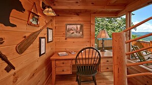 A wooden cabin interior with a desk, chair, and a painting on the wall. - Above It All #38 (Sevierville)