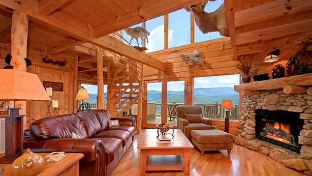 A wooden cabin interior with a leather sofa, a stone fireplace, and a view of the mountains. - Above It All #38 (Sevierville)