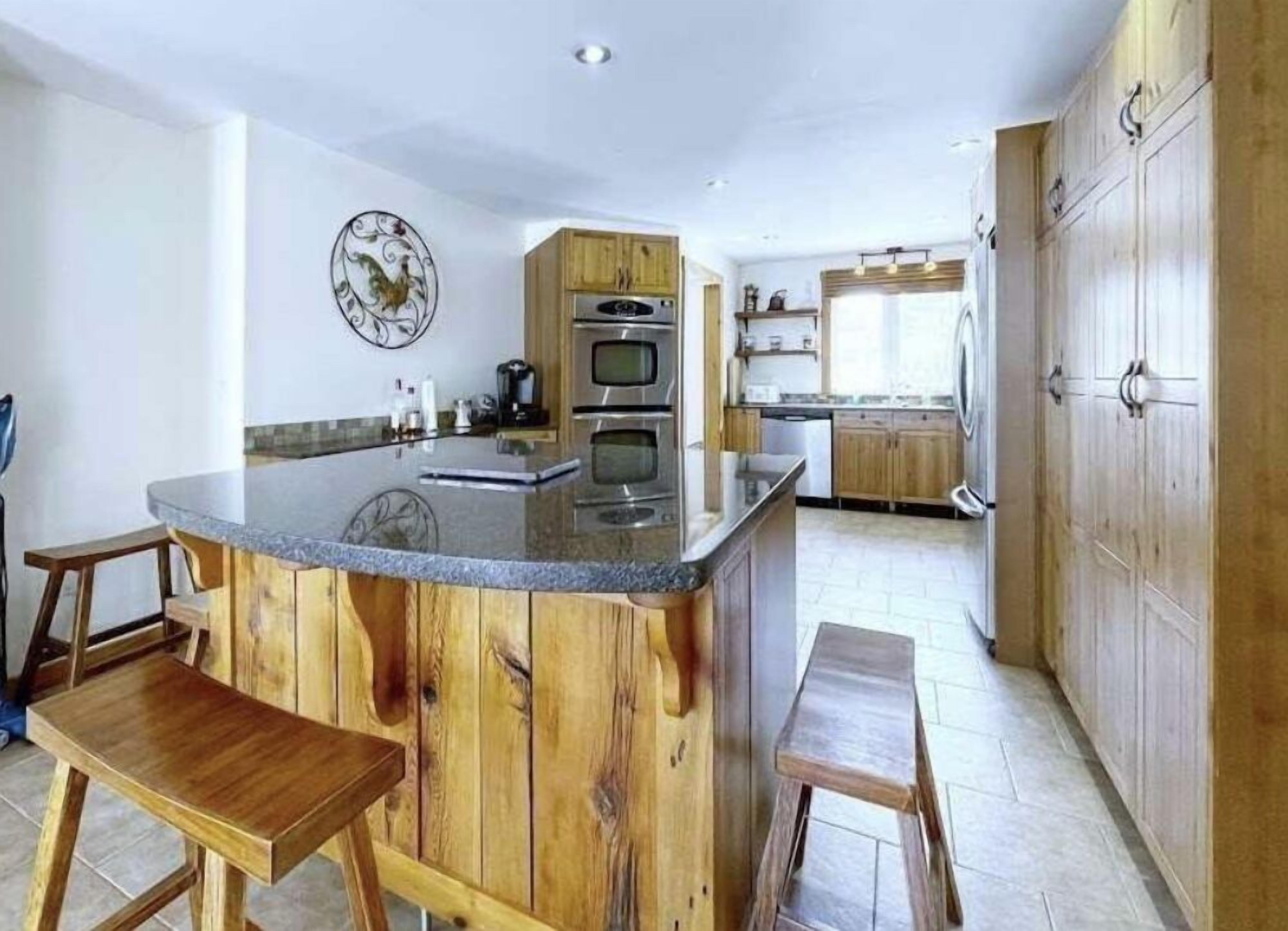 A kitchen with a wooden island, built-in oven, and a decorative rooster wall art.