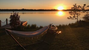 Eine Hängematte und ein Stuhl am Ufer eines ruhigen Sees bei Sonnenuntergang.