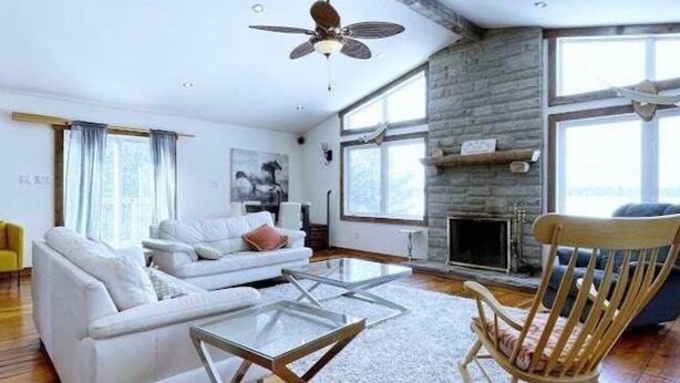 Ein modernes Wohnzimmer mit einem weißen Sofa, einem Glastisch, einem Holzschaukelstuhl und einem Kamin.