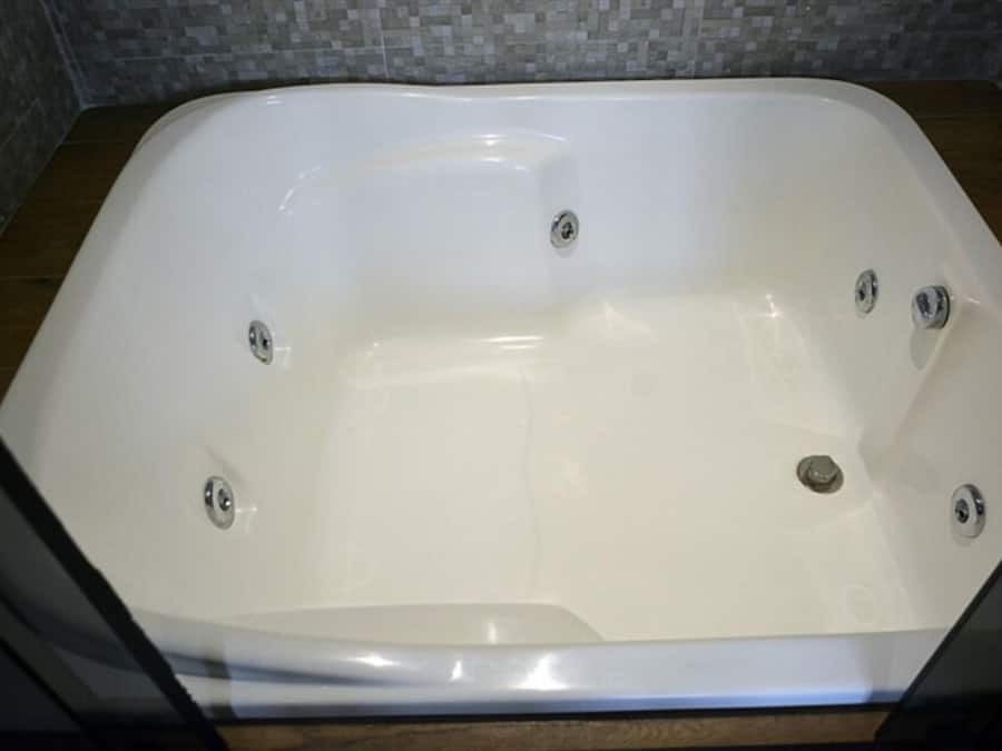 A rectangular bathtub with four faucets, set against a tiled wall.
