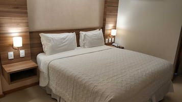 A hotel room with a large bed, wooden headboard, bedside lamps, and an air conditioning unit.