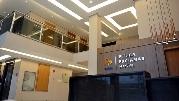 A modern hotel lobby with a reception desk, glass railings, and a sign for 'PITUBA PRAJAMAR HOTEL'. - Pituba Praiamar Hotel (Salvador)