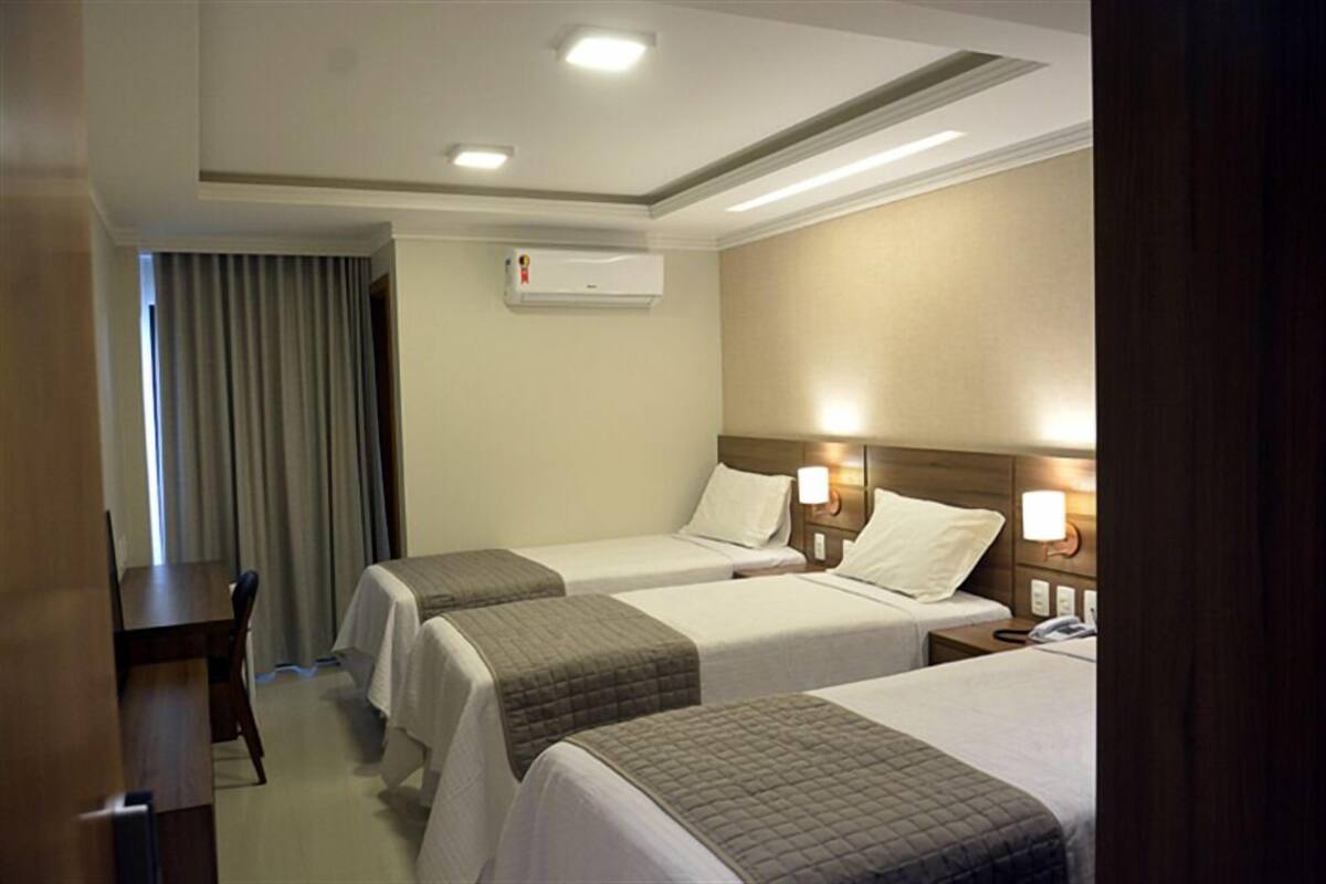 Habitación de hotel con dos camas individuales, un escritorio, una silla, un equipo de aire acondicionado y una ventana con cortinas.
