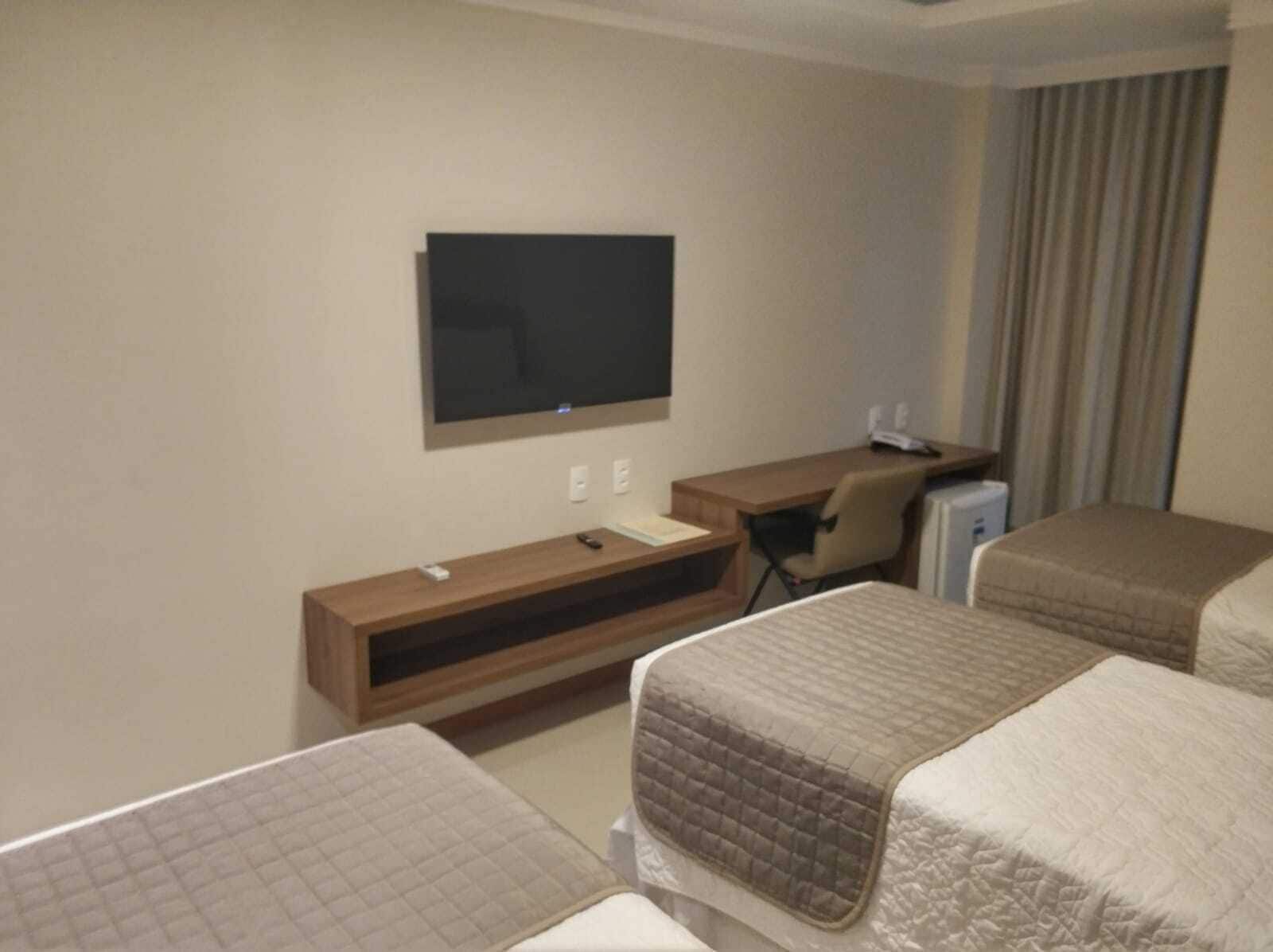 Habitación de hotel con una televisión montada en la pared, un escritorio con una silla y dos camas con cabeceros.