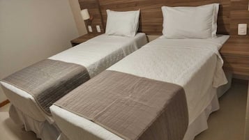 Quarto de hotel com duas camas de solteiro, cada uma com travesseiro e cobertor.
