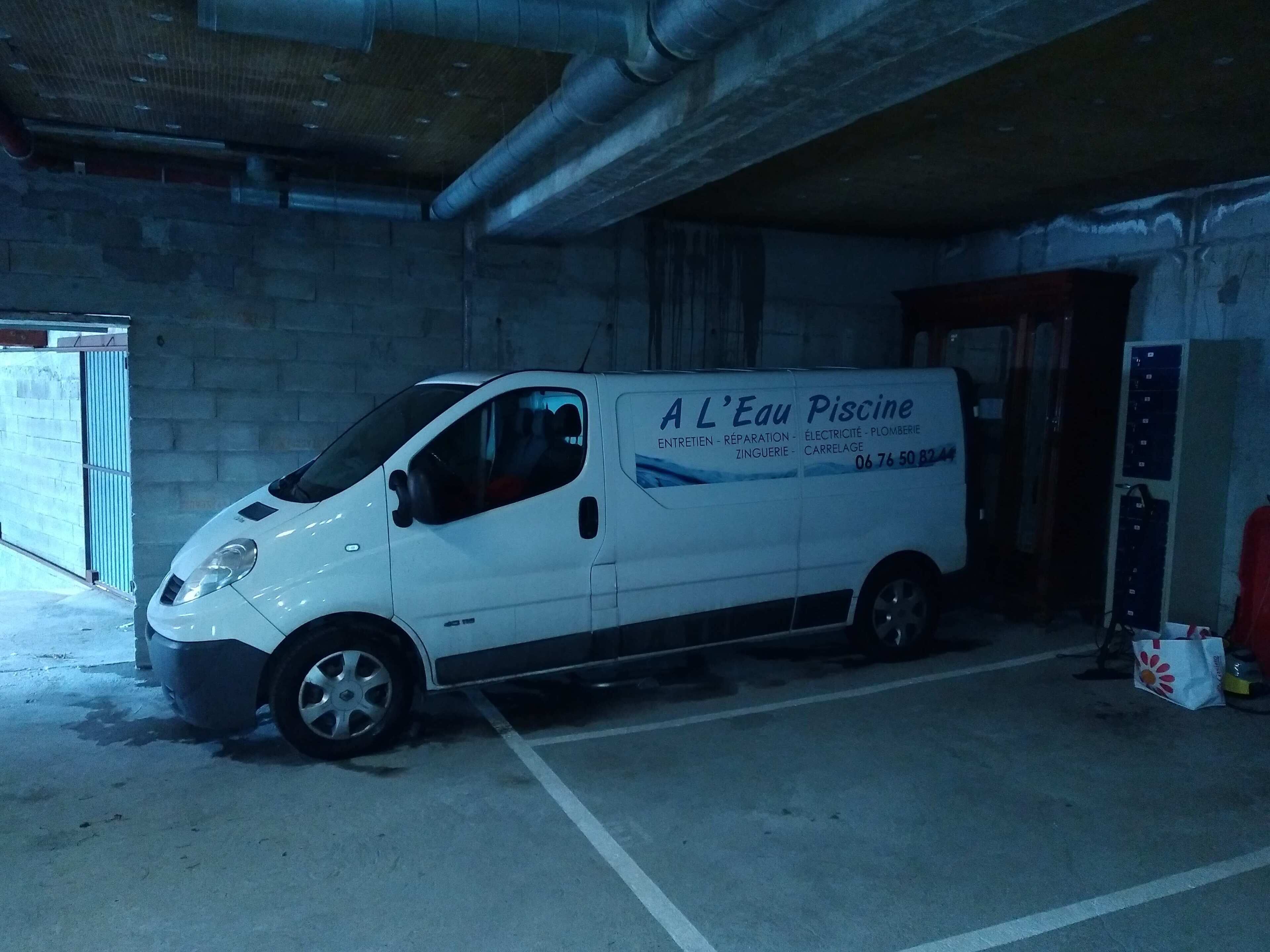 A white van parked in a dimly lit garage with a brick wall and concrete floor.