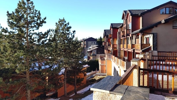 A row of multi-story buildings with balconies, wooden railings, and a snowy ground.