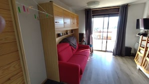 A living room with a red sofa, wooden cabinets, a television, and a sliding glass door leading to an outdoor area.