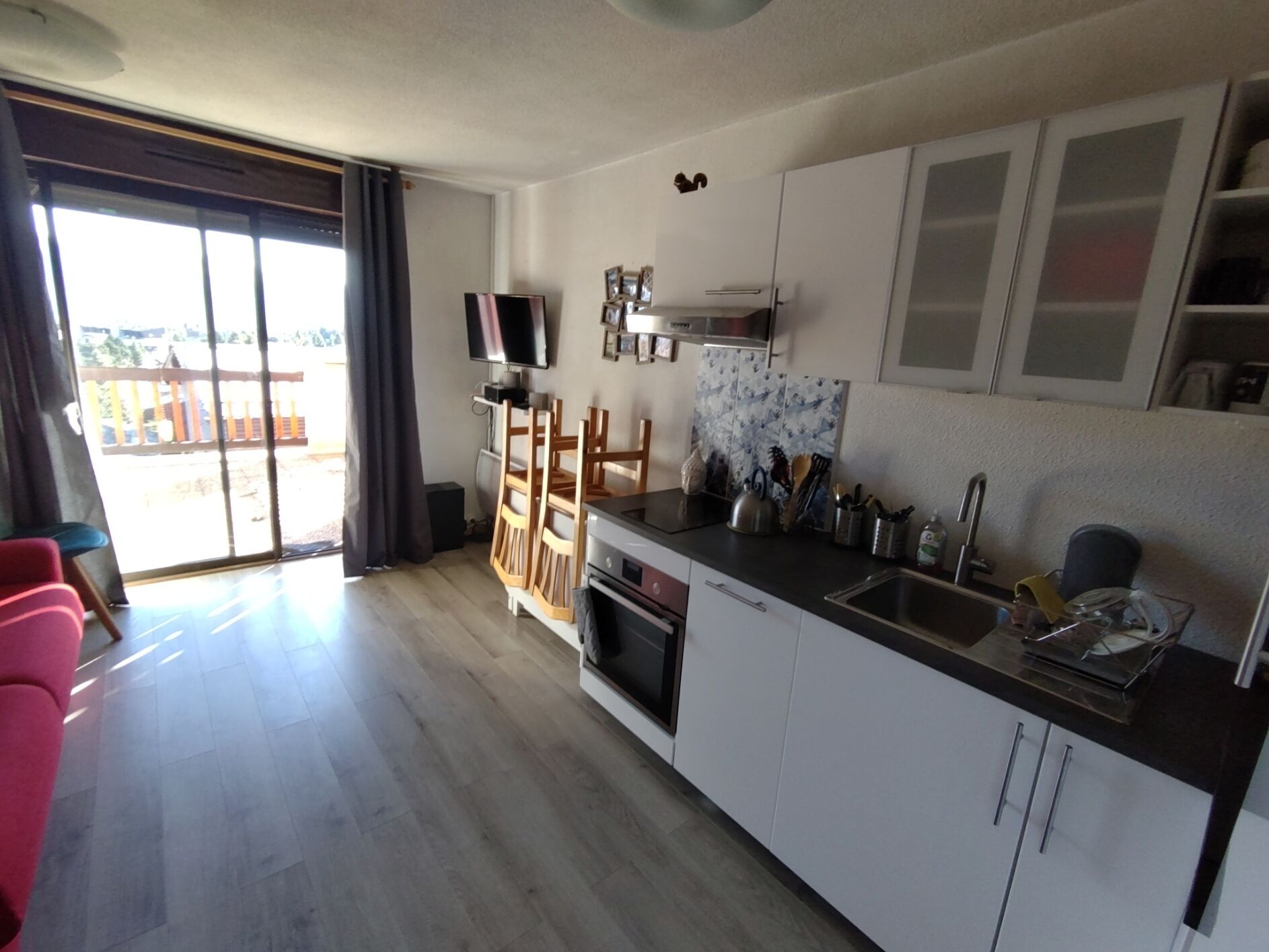 A modern kitchen with a flat-screen TV, wooden chairs, and a dining area with a view of the outside.