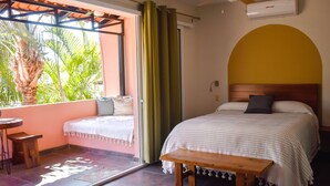 Camera da letto con un letto, una panca in legno, un tavolino e vista su palme attraverso una finestra.