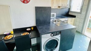 Cocina compacta con lavadora, un reloj y zona de comedor con desayuno.