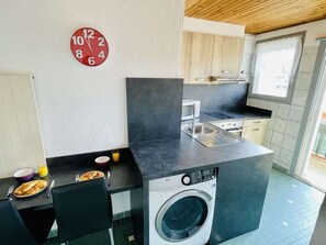Une cuisine compacte équipée d’un lave-linge, d’une horloge et d’un coin repas où le petit-déjeuner est servi.