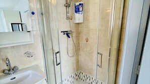 Ducha en esquina con mampara de vidrio, lavabo integrado y panel de control.