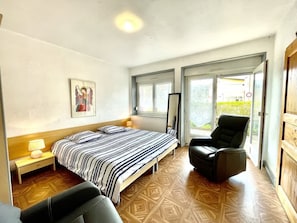 A bedroom with a bed, a chair, a nightstand, and a window.