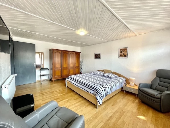 A bedroom with a bed, a chair, a wardrobe, and a desk.