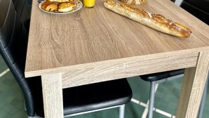 A wooden dining table with breakfast items including croissants, juice, and a fruit basket. - Angèle (Bains-les-Bains)