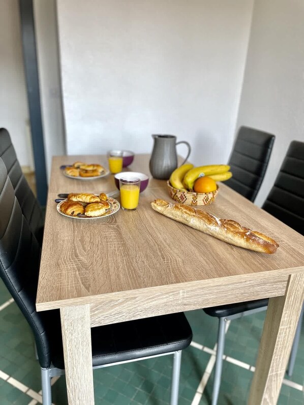 Una mesa de madera para comer con alimentos para el desayuno, como cruasanes, jugo y una cesta de frutas.