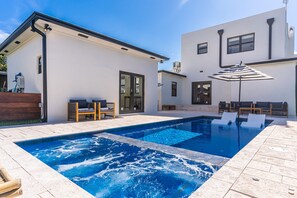 Ein moderner Poolbereich mit Whirlpool, Sitzgelegenheiten im Freien und blauem Himmel.