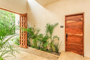 A wooden door with a number plate, a wooden lattice structure, and various green plants.