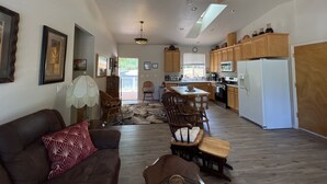 A spacious living area with a dark brown sofa, a wooden coffee table, and a dining area with wooden chairs and a small table. A ceiling fan and a window with blinds are visible. - Rural home wheelchair accessible, pet friendly close to River & lake & I-80. (Meadow Vista)