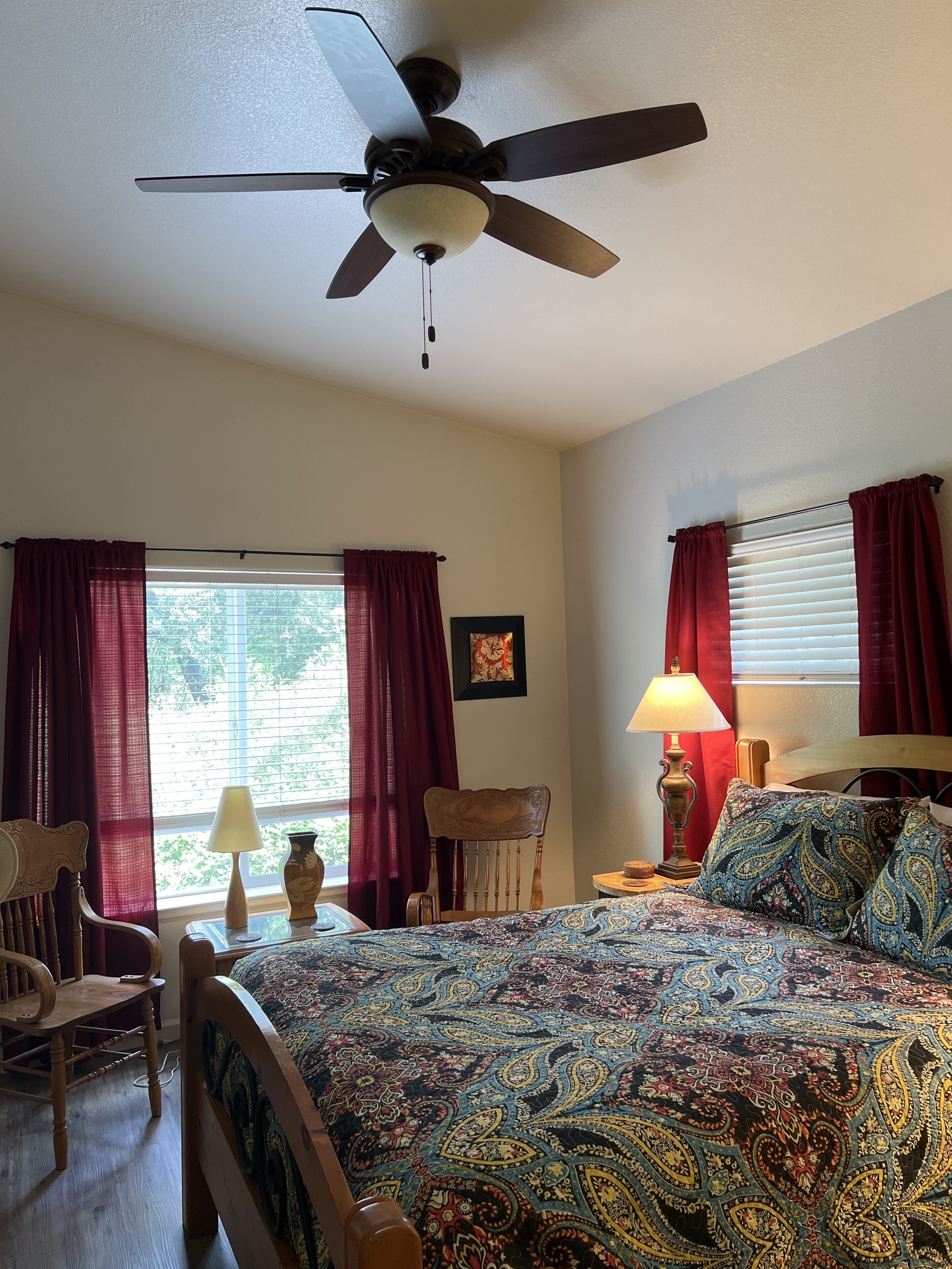 A bedroom with a bed, a chair, a table, a lamp, and a ceiling fan.