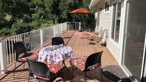 A covered patio with a table and chairs, a grill, and a view of the surrounding trees. - Rural home wheelchair accessible, pet friendly close to River & lake & I-80. (Meadow Vista)