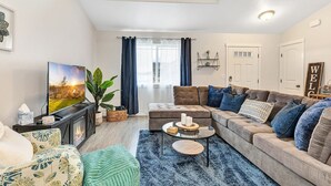 A modern living room with a large flat-screen TV, a sectional sofa, a coffee table, and a fireplace.