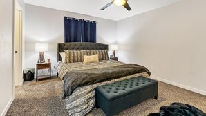 A bedroom with a bed, two bedside tables, a floor lamp, a ceiling fan, and a window with curtains.