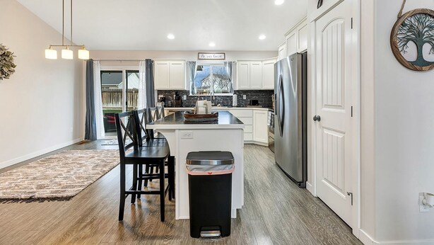 A modern kitchen with white cabinets, a stainless steel refrigerator, and a dining area with a black table and chairs.