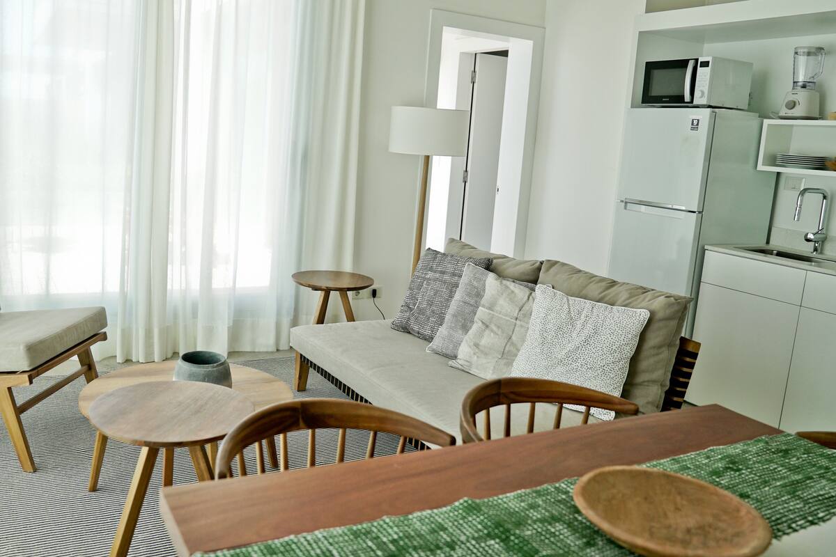 A modern living room with a sofa, chairs, a dining table, and a kitchen area with appliances.
