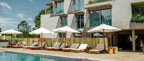 Un hotel moderno con piscina, tumbonas y sombrillas.