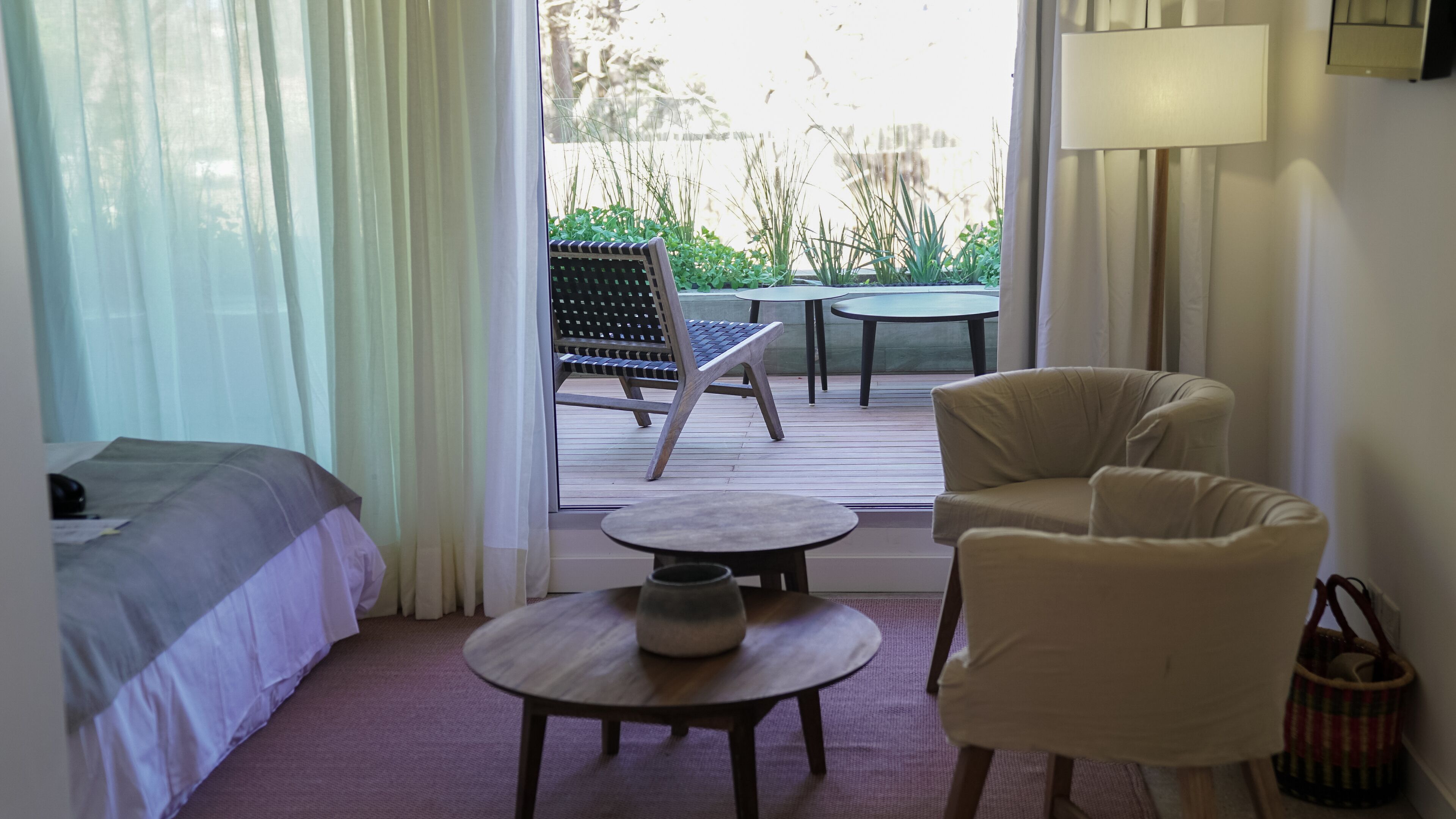 A hotel room with a bed, a round table, a chair, and a view of an outdoor patio with a table and chairs.