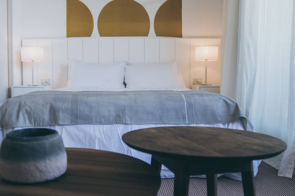 A hotel room with a large bed, two bedside lamps, a round table, and a decorative vase.