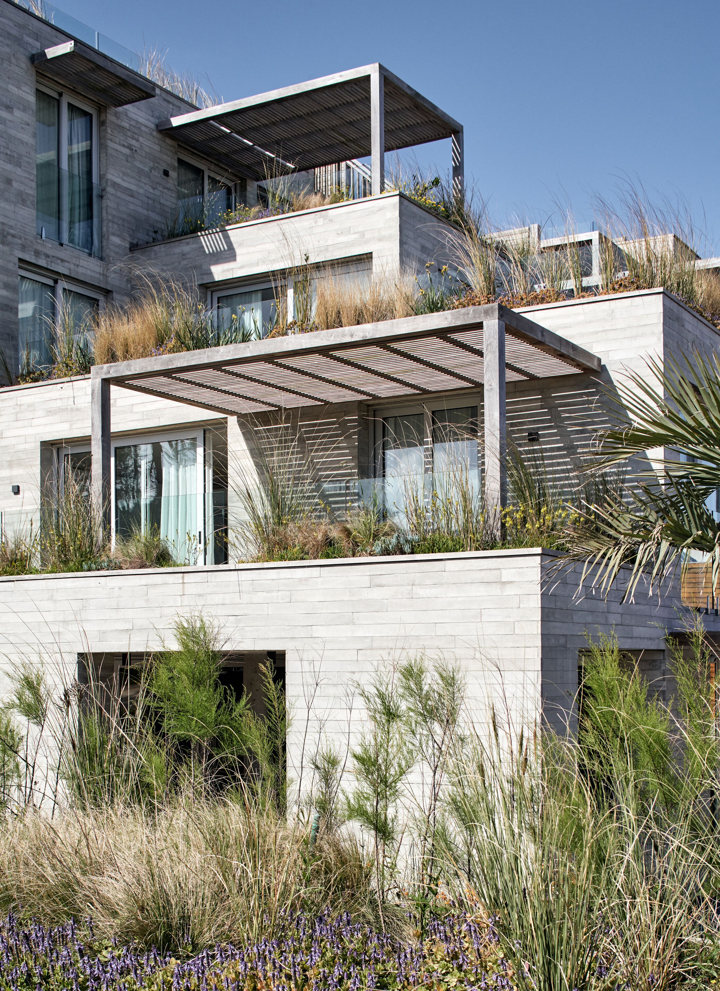 A modern multi-story building with a flat roof, large windows, and a covered outdoor area.