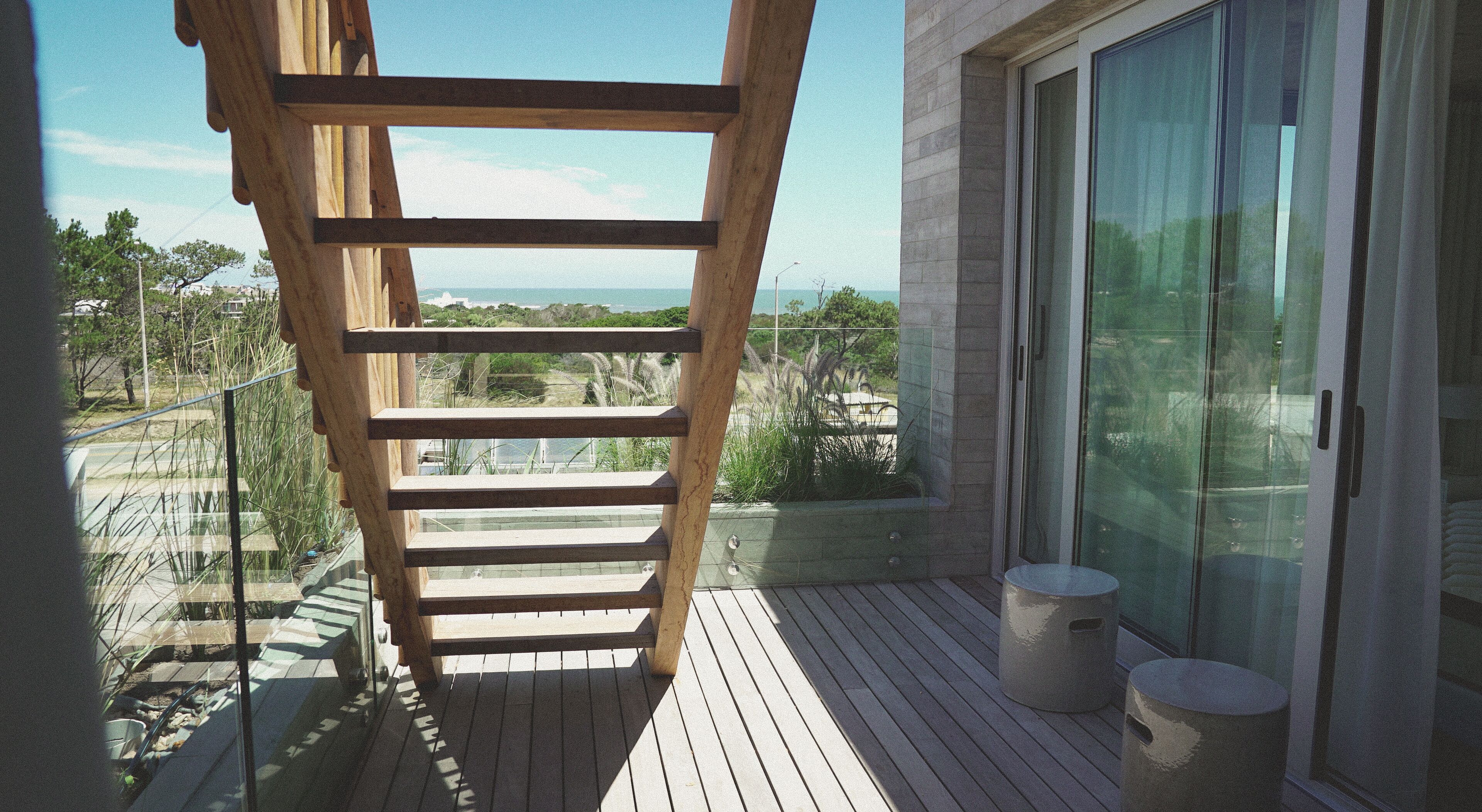 Une terrasse en bois dotée d’une balustrade en verre, offrant une vue sur un paysage côtier.