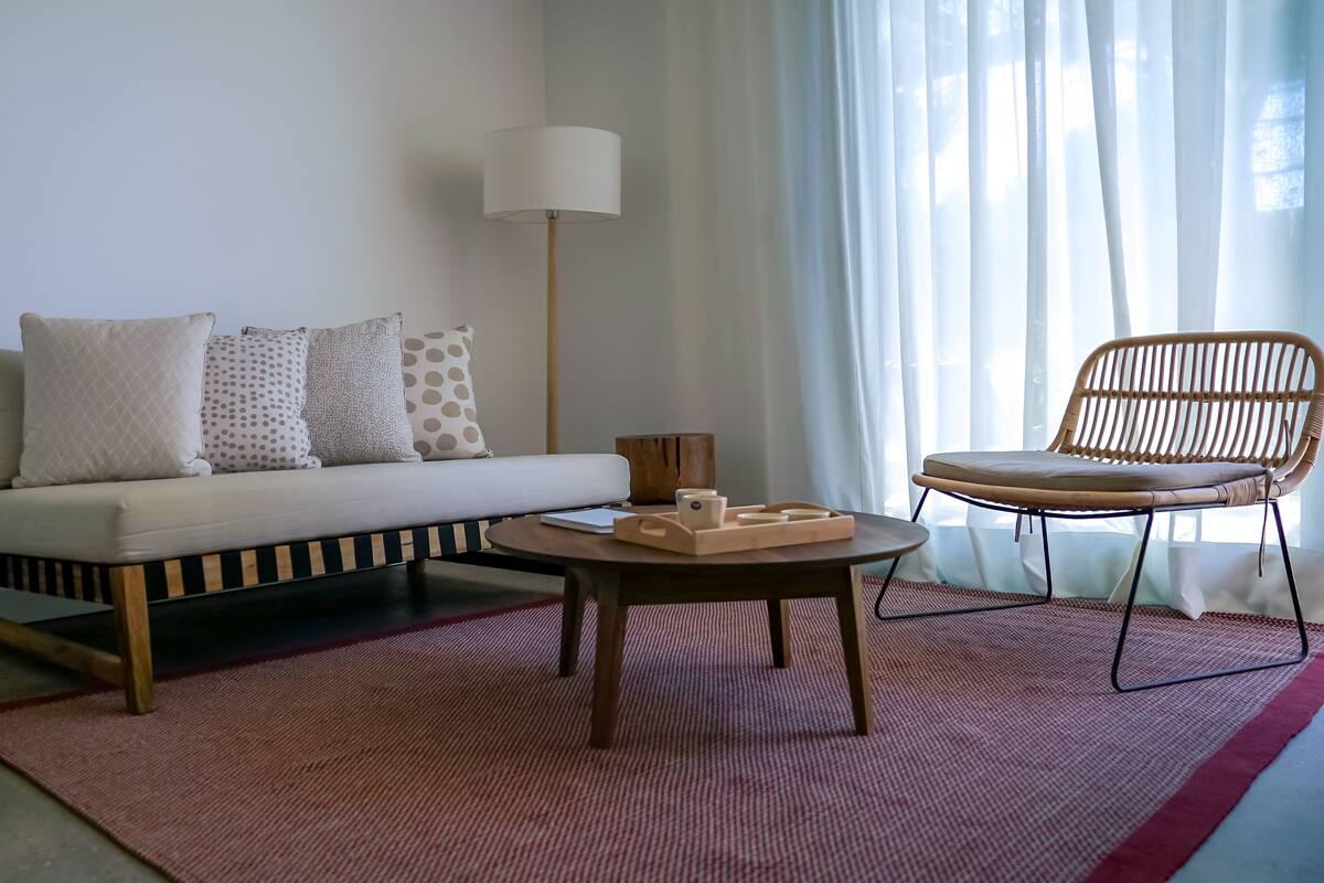 A living room with a sofa, a round coffee table, a wicker chair, and a lamp.