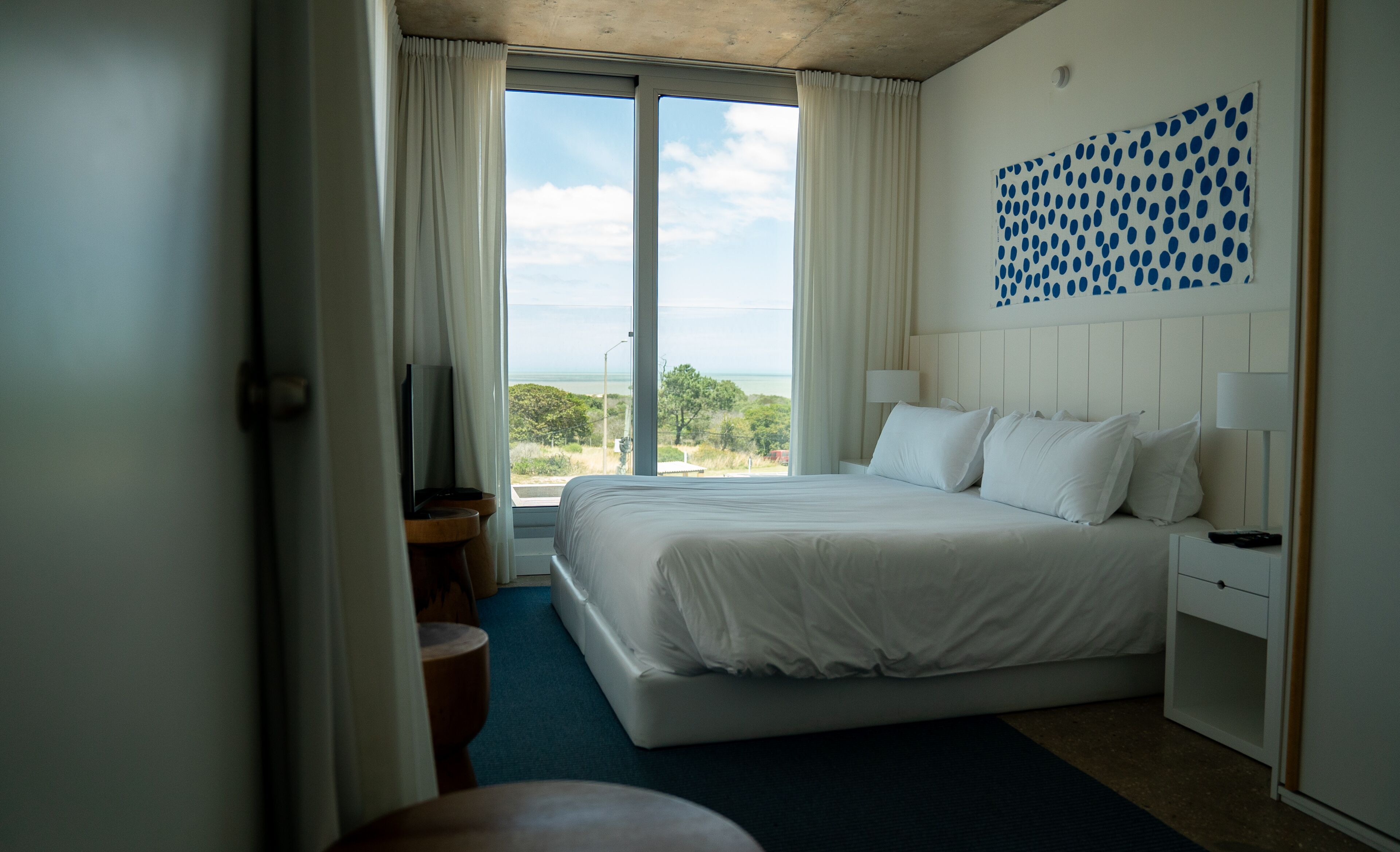 A hotel room with a large bed, a TV, a desk, and a view of the ocean.