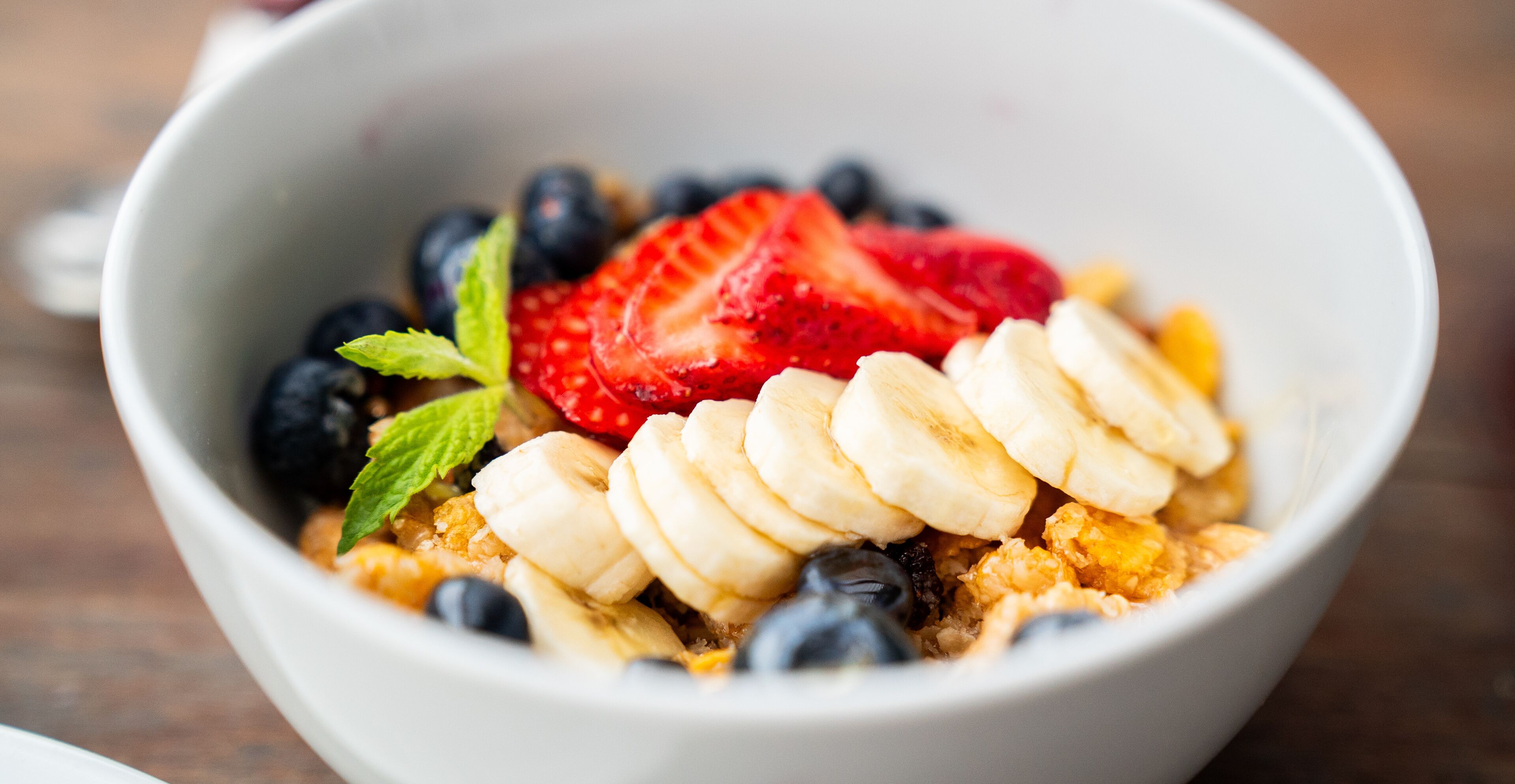 A bowl of cereal with sliced bananas, strawberries, and blueberries.