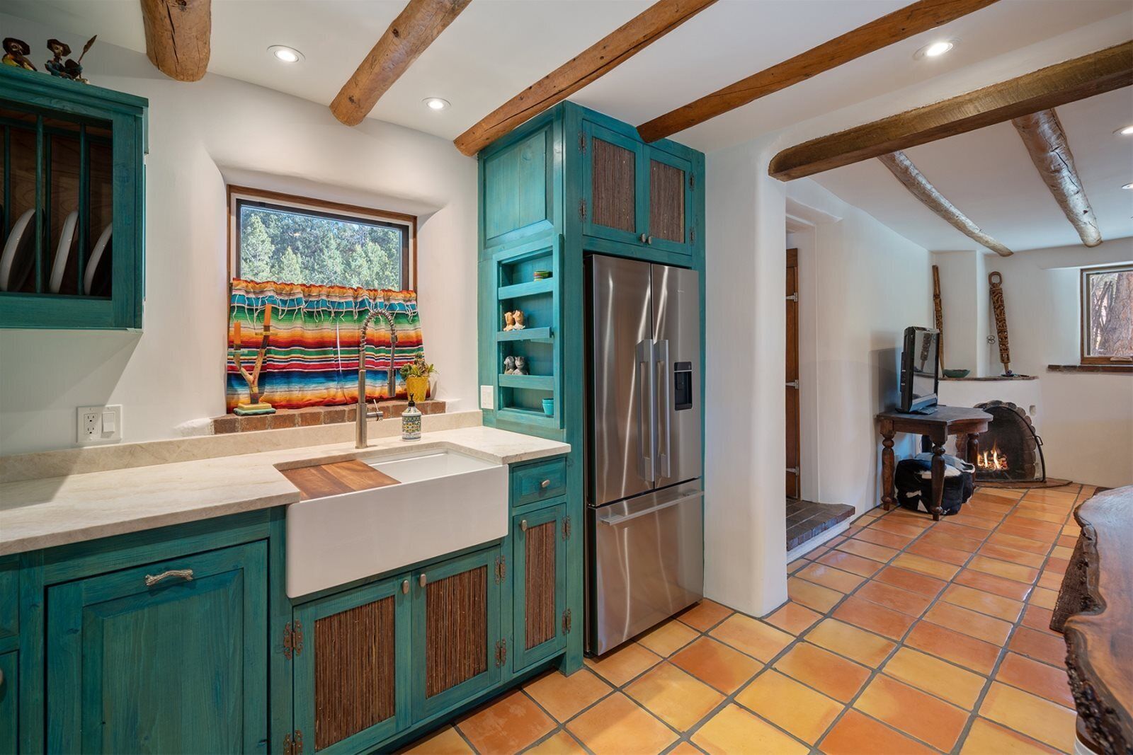 A kitchen with teal cabinets, a stainless steel refrigerator, and a window with a colorful curtain.