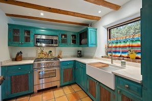A kitchen with teal cabinets, a stainless steel stove, and a window with colorful curtains. - Dancing Hare - Colorful and Inviting Tesuque Home Right Next to Bishop`s Lodge (Santa Fe)