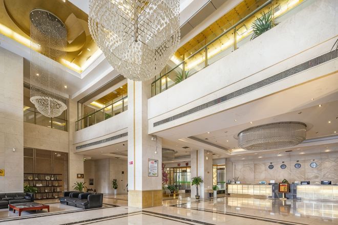 A spacious lobby with a high ceiling, chandeliers, a reception desk, and seating areas.