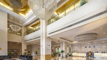 A spacious lobby with a high ceiling, chandeliers, a reception desk, and seating areas.