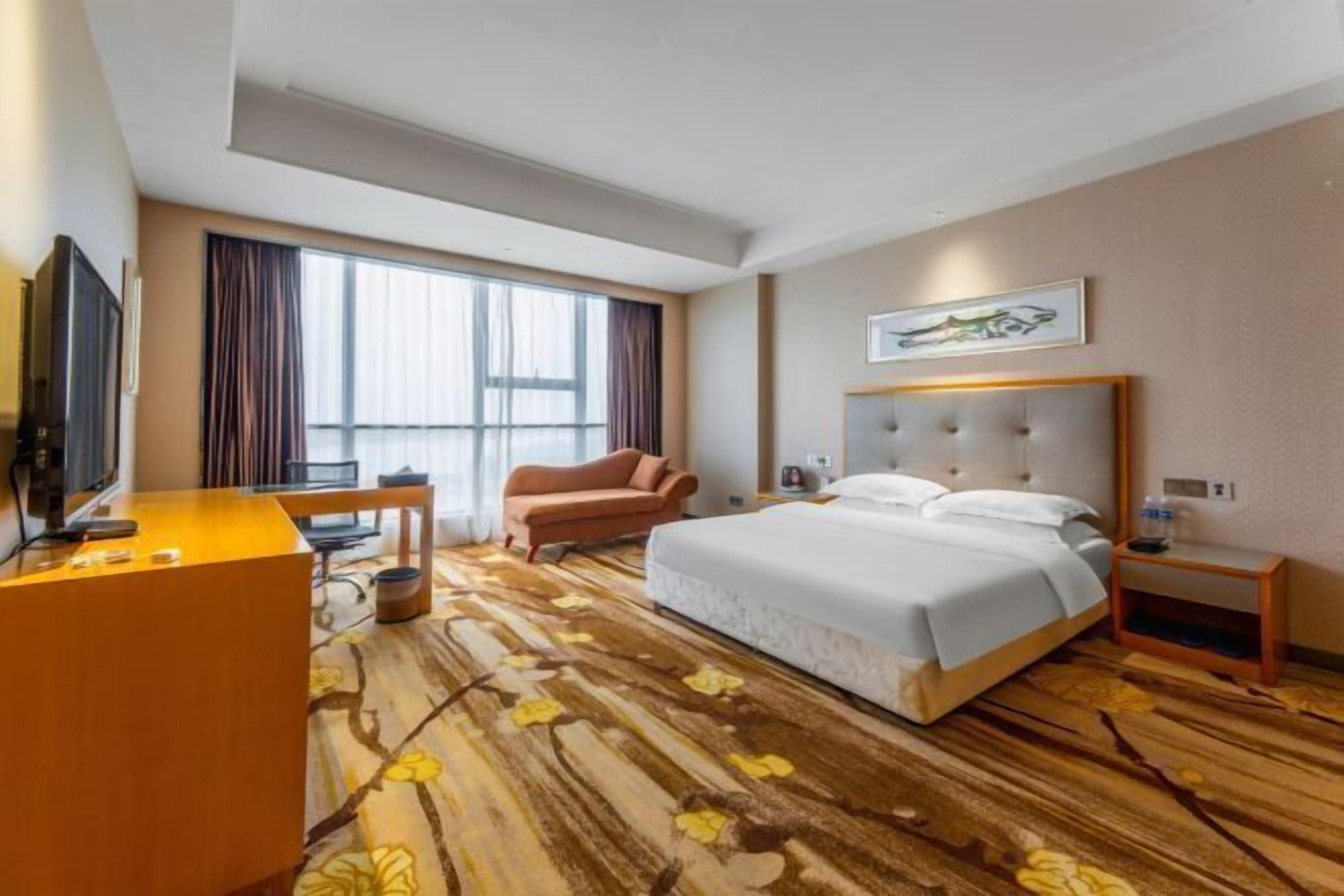 Una habitación de hotel con una cama grande, un escritorio, una silla y un televisor.