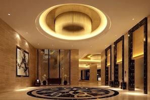 En modern hotellobby med en rund lampa i taket, en receptionsdisk och ett mönstrat golv.