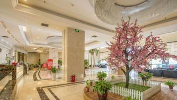 A hotel lobby with a reception desk, a large column, and a decorative tree with pink blossoms.